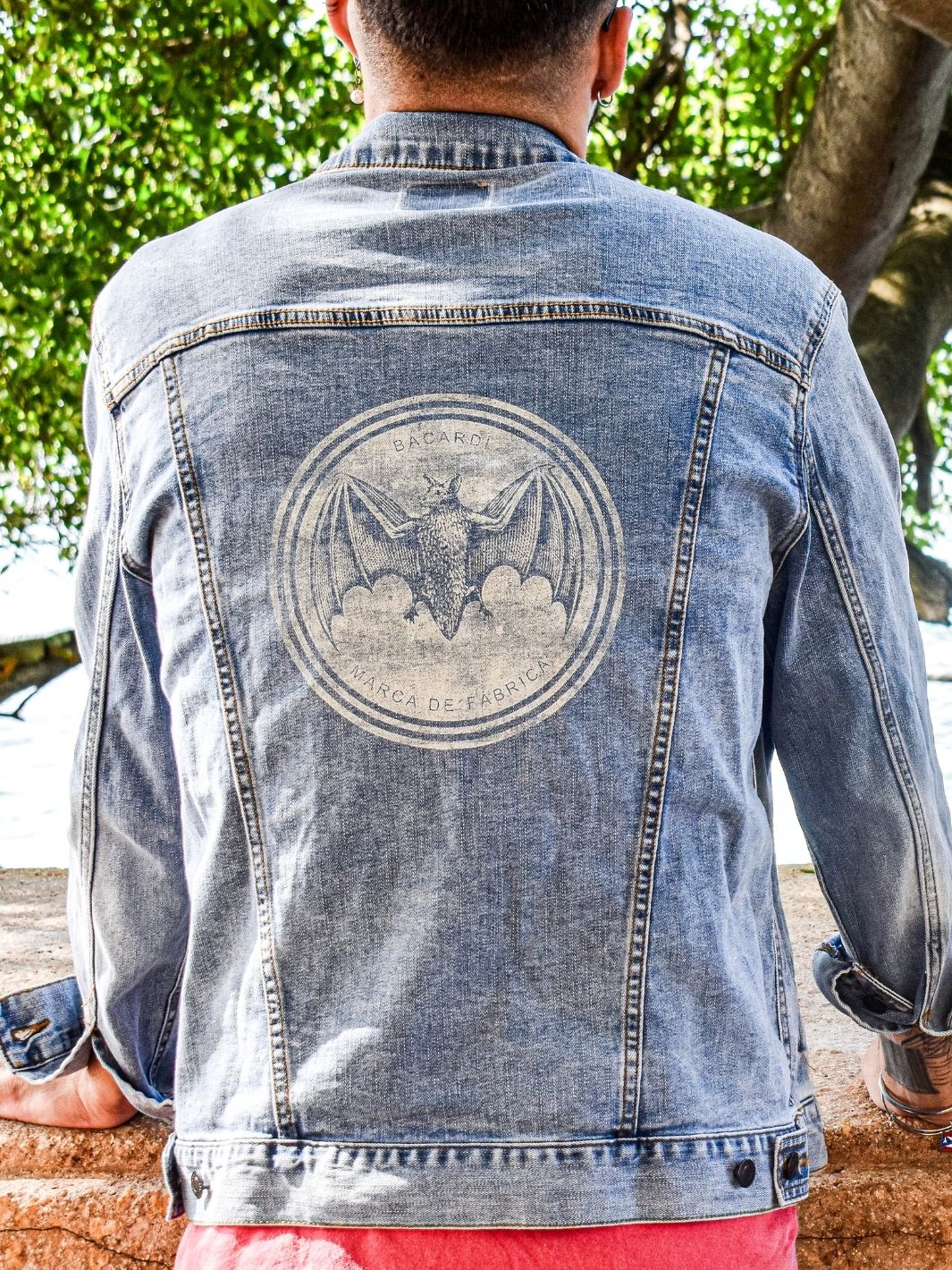 Outdoor view of Bacardi denim jacket back, featuring large embroidered bat logo in center